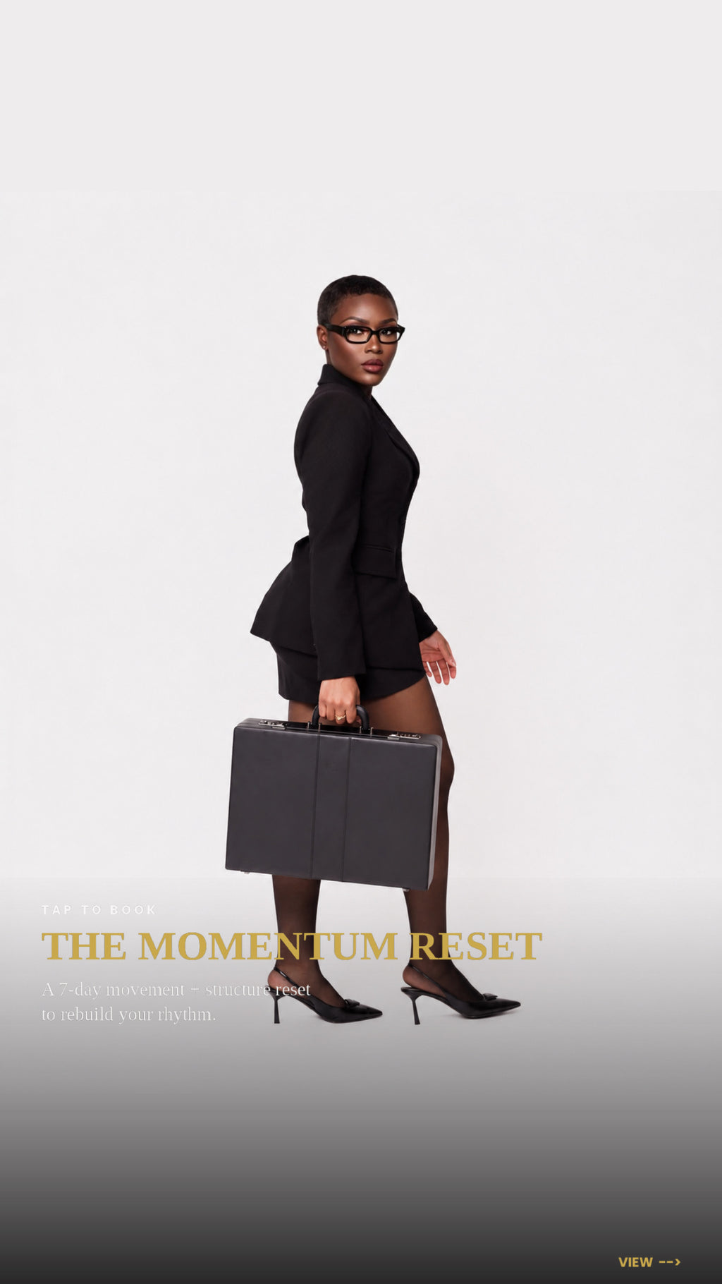 A woman in a black peplum-style blazer and matching skirt walks while carrying a dark gray briefcase, wearing black heels and glasses. The background is a clean light gray studio backdrop with the text 'THE  BODY ERA MOMENTUM RESET' near the bottom.